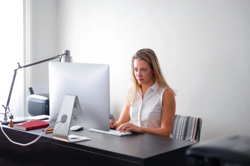 A woman sits at a desk, focused on her computer screen while typing.