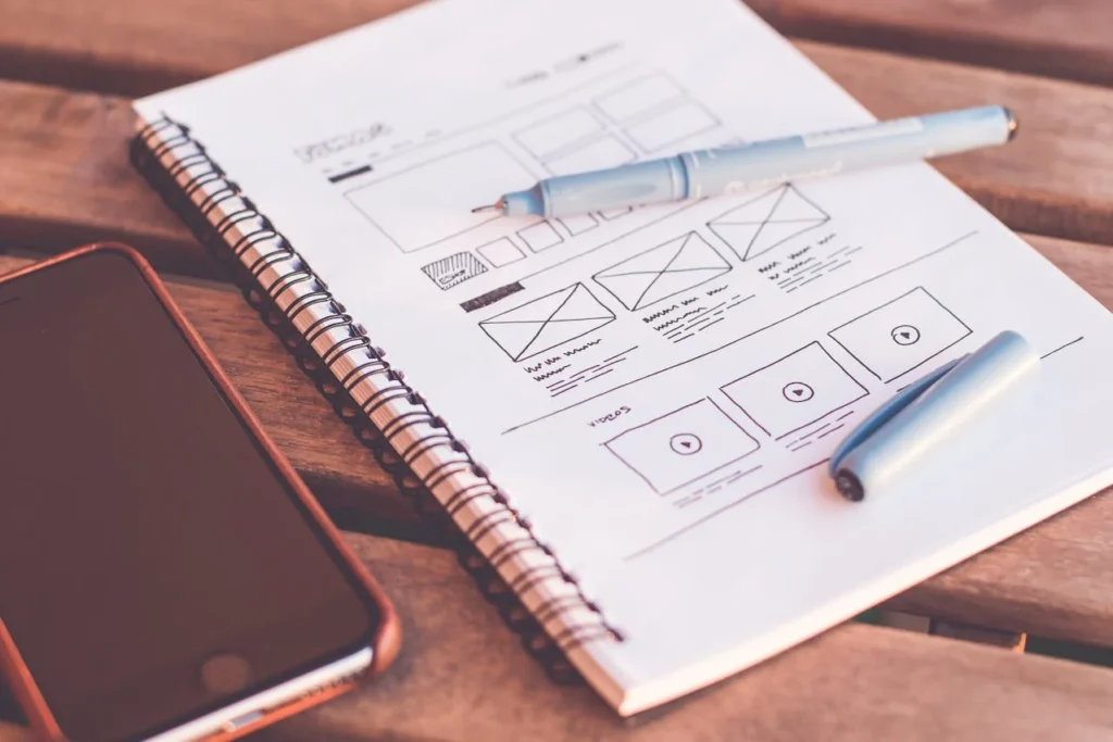 A notebook, pen, and smartphone arranged on a wooden table, showcasing a workspace setup.